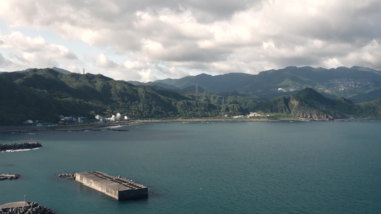4K Drone aerial shot slowly panning left to reveal coastal landscape with blue ocean, shoreline, and harbor. Scenic seaside view with calm water and natural horizon, good weather