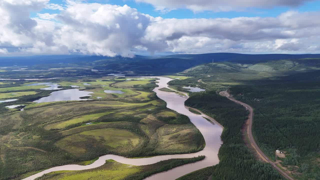 Dramatic aerial view of meandering river flowing through lush green landscape under dynamic cloudy sky in Alaska, perfect for travel inspiration and outdoor adventure content