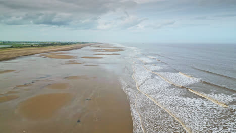 Aerial-video-footage-of-a-coastal-beach-scene-with-ocean,-sand-dunes-and-crashing-waves
