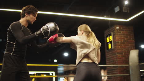 Angry-sport-woman-training-with-coach-at-gym.-Fit-girl-fighting-on-boxing-ring