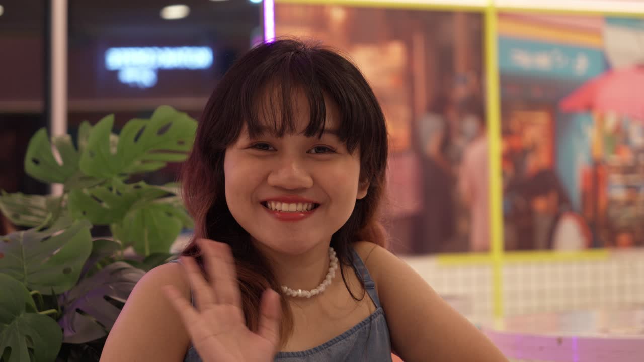 una joven indonesia mira a su alrededor, buscando a alguien. cuando los encuentra, los saluda.