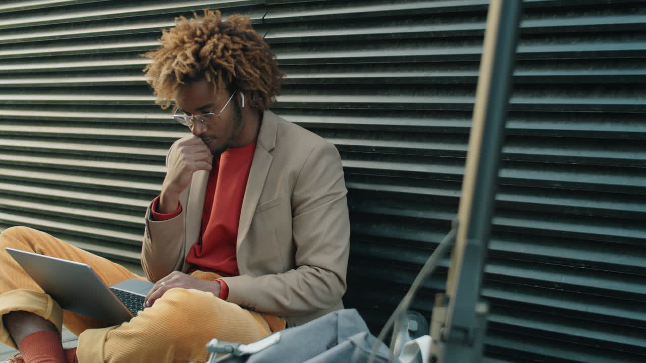 African American Man Sitting on Street and Working on Laptop
