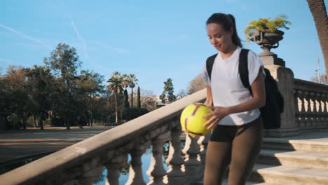 jugadora de fútbol mujer con mochila y pelota en las manos corriendo por las escaleras en el parque de la ciudad a toda prisa.