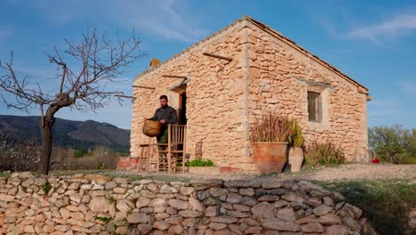 Antigua-Casa-De-Piedra-En-Medio-De-Olivares-Mediterráneos,-Un-Hombre-Prepara-La-Mesa-Para-El-Almuerzo-A-Principios-De-La-Primavera