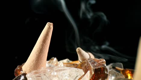 close-up of unlit incense cone in a decorative rock garden, a lit cone w- smoke billowing in off focus