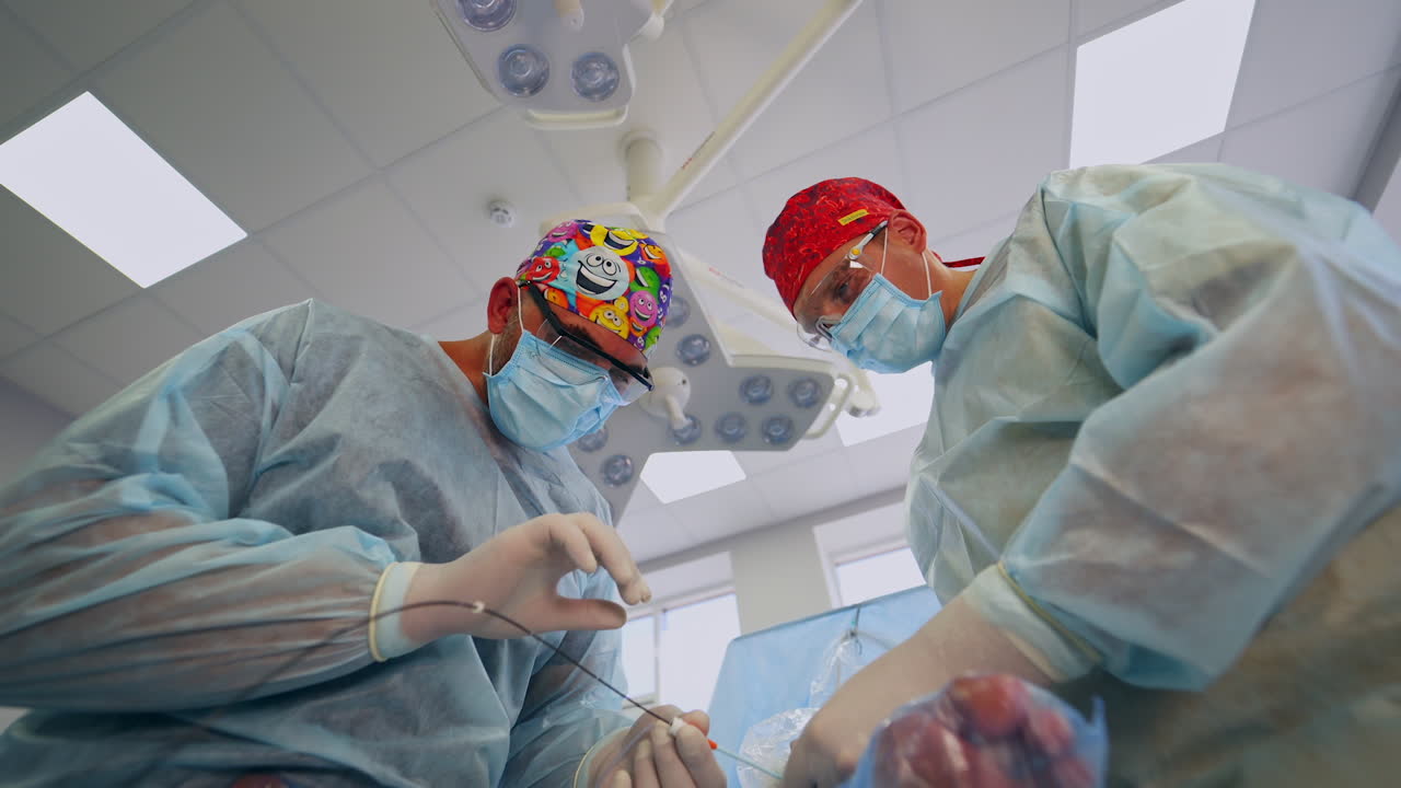 Phlebology specialist use tools at operation on patient's leg. Adult male doctors perform surgery on veins. Low angle view.