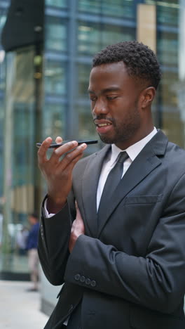 vertical video shot of young businessman wearing suit talking on mobile phone using built in microphone standing outside offices in the financial district of the city of london uk shot in real time 3