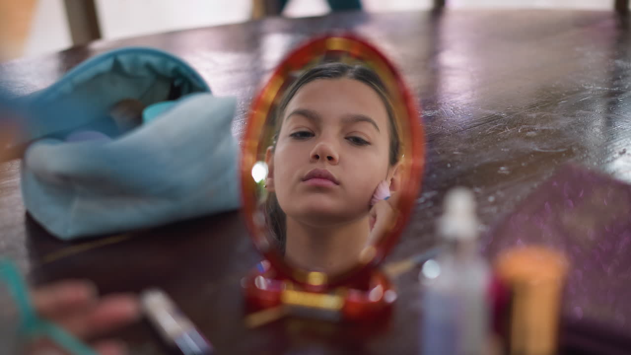 화장품 제품이 밝은 실내 환경에서 테이블에 보이는 브러쉬를 사용하여 얼굴에 메이크업을 적용하는 동안 거울에서 젊은 여자의 반사에 대한 근접 시각