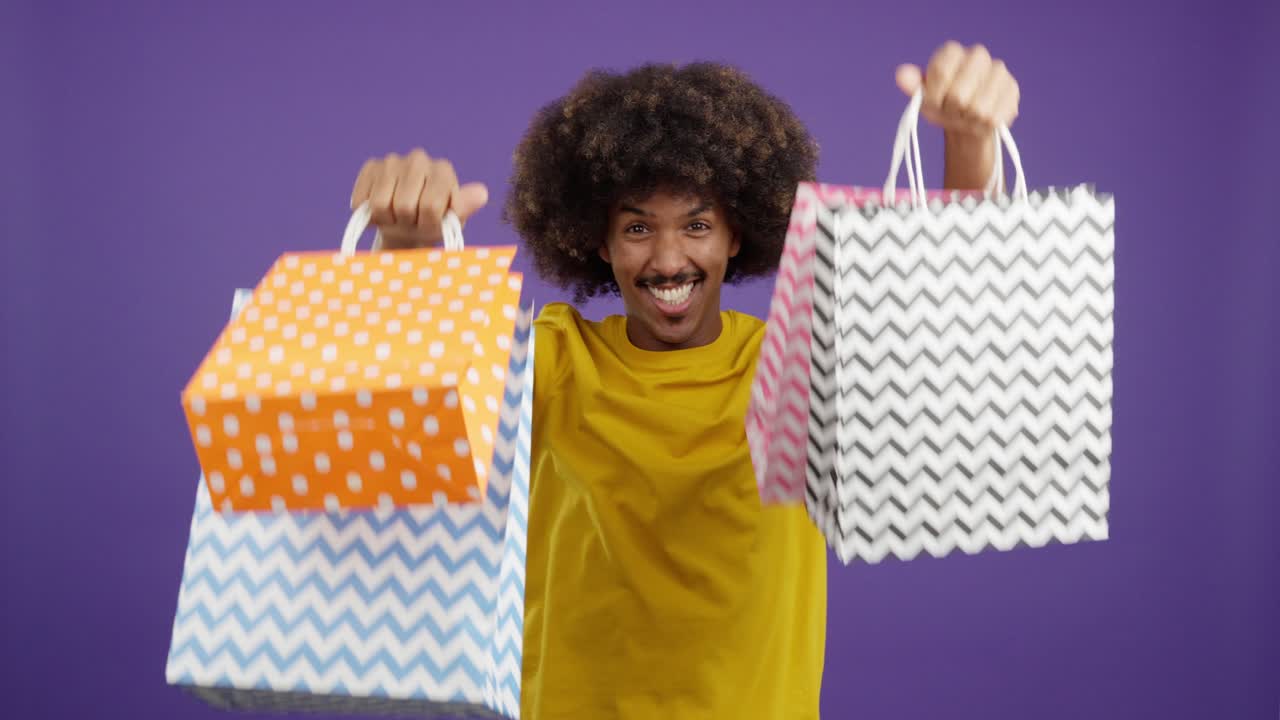 Happy Man with Afro Celebrates Shopping with Bags on Purple Background