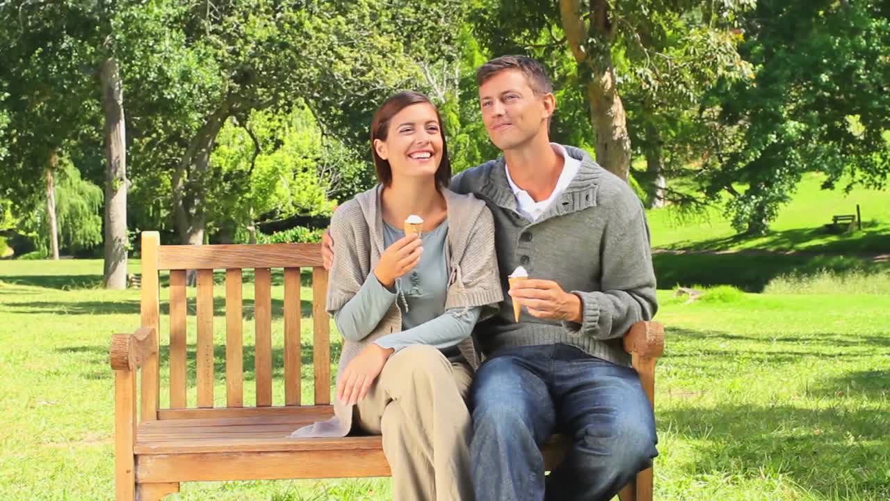 젊은 부부 가 공공 벤치 에서 아이스크림 을 먹고 있다