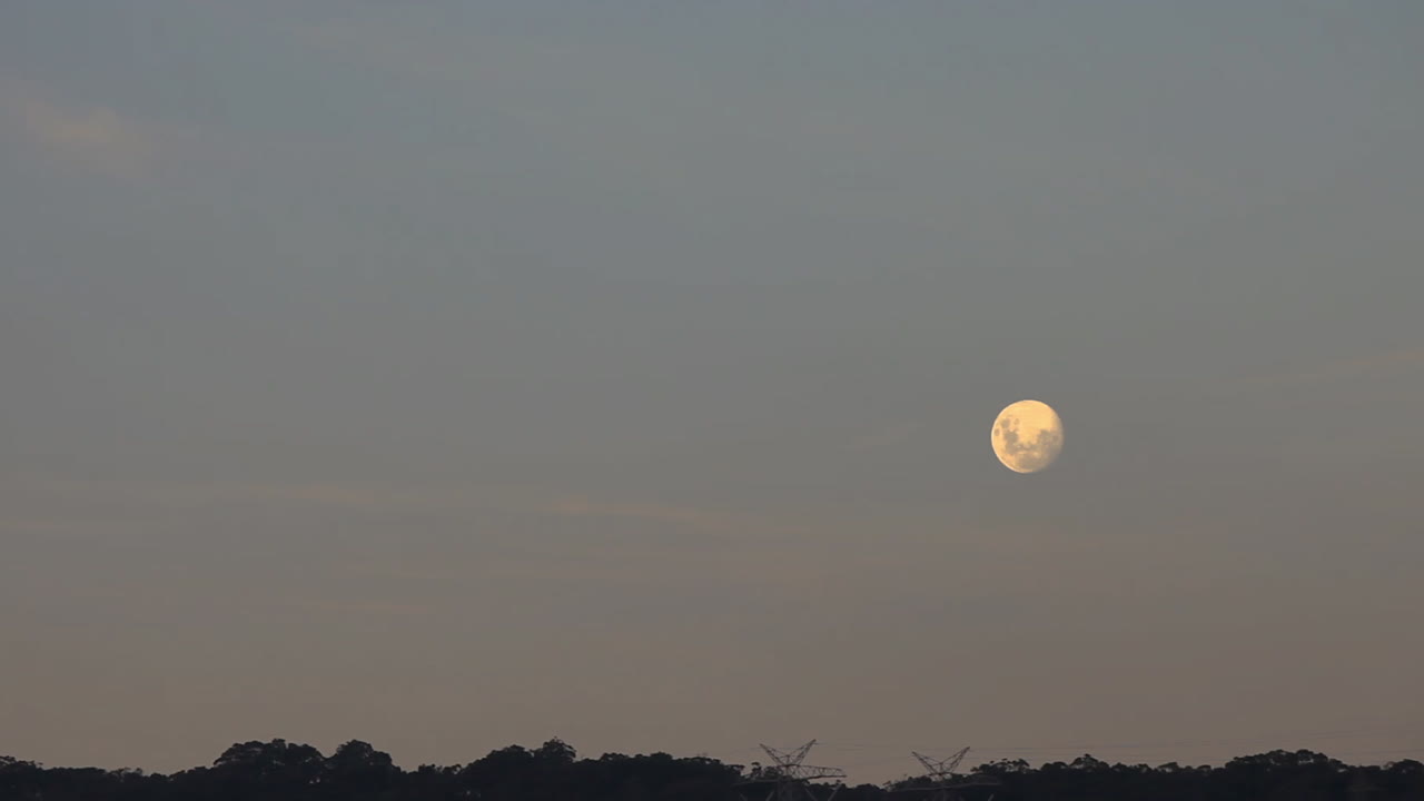 Full moon timelapse moving higher into the sky during dusk evening light.