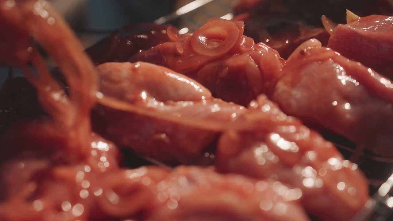 Primo piano di pollo marinato sulla griglia, lo chef del campeggio lo spennella con cipolla affettata, pezzi sfrigolanti su un falò di braci, luce dorata calda, mani che sistemano la carne sulla graticola, glassa saporita e ambiente fumoso.