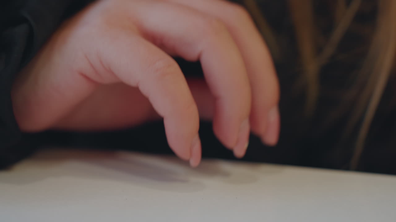 Mano di donna caucasica in primo piano sul tavolo, dita in bilico sulla superficie, unghie naturali e polpastrello, sottile tremore e intento furtivo, messa a fuoco superficiale con grana cinematografica, atmosfera nervosa e silenziosa che suggerisce.