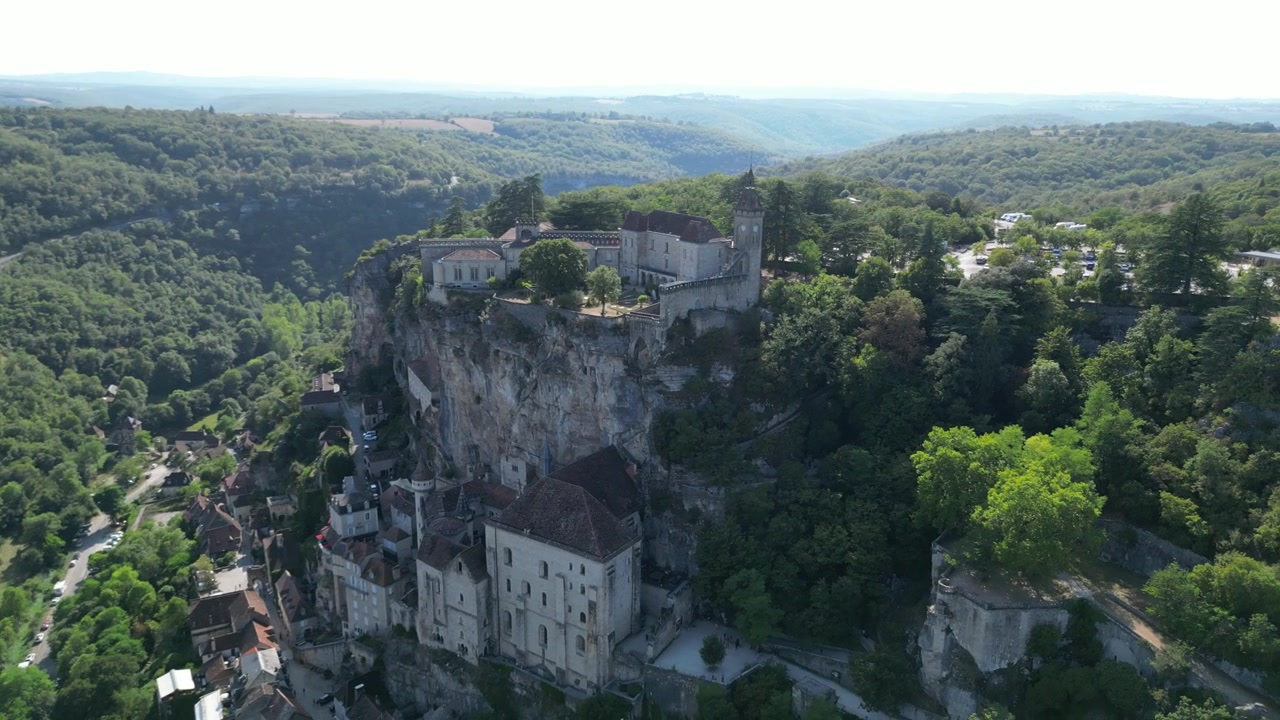 Vue aérienne par drone de la petite ville médiévale de Rocamadour, située sur une falaise rocheuse dans la campagne française, avec son château et sa cathédrale, encerclée par une forêt de montagne verdoyante.