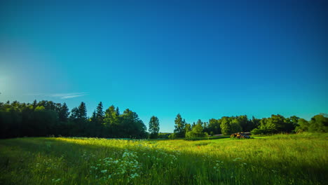 Day-to-night-timelapse-of-white-clouds-passing-by-over-a-green-meadow-surrounded-by-trees