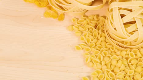 various pasta types and grains arranged on a light wooden surface with warm lighting