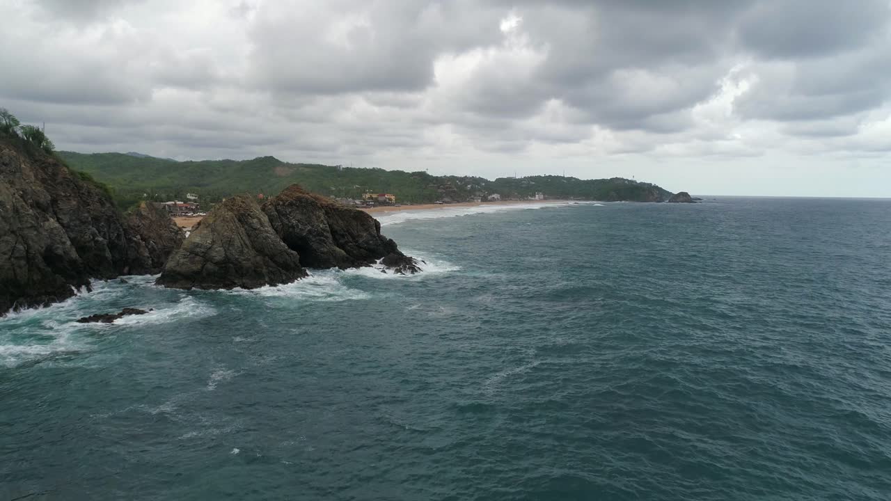 Ripresa aerea con drone di una grande formazione rocciosa con la spiaggia di Zipolite sullo sfondo, Oaxaca
