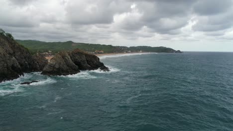 Aerial-drone-shot-of-a-big-rock-formation-with-Zipolite-beach-behind,-Oaxaca