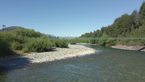 Aerial-parallax-of-Rio-Azul-river-and-elevated-bridge-surrounded-by-trees-and-mountains,-Patagonia-Argentina