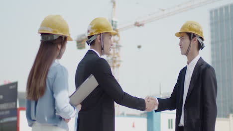 business building partners shaking hands in helmets with documents checking plans at construction site