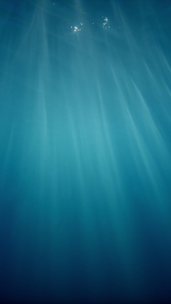Sunlight beams filter through the deep, crystal-clear, blue-turquoise water, casting a beautiful curtain of reflections