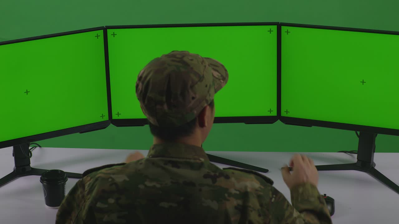 vista trasera de feliz hombre asiático soldado celebrando mientras trabajaba con simulacro de múltiples monitores de computadora en el estudio de pantalla verde