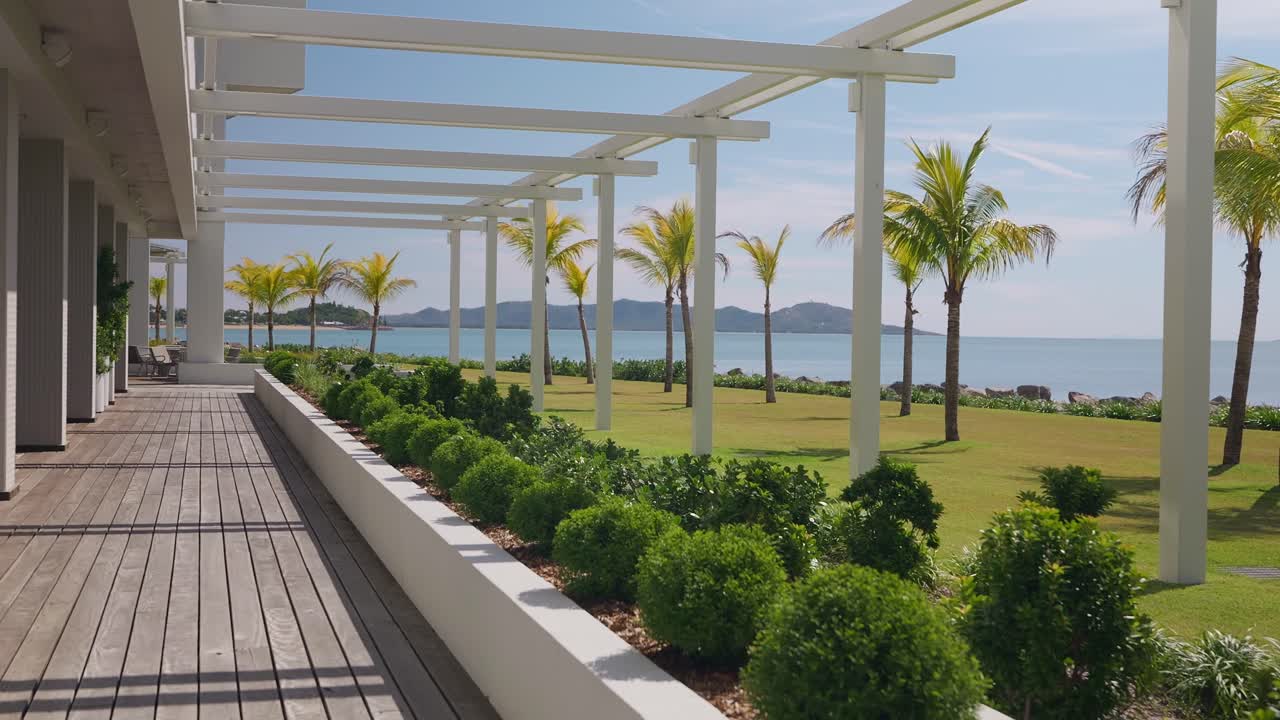 Pan right, The stunning tropical beach front view at a new waterfront hotel in North Queensland, Australia, looking out at the palm trees, beach, island in background from the vast wooden deck