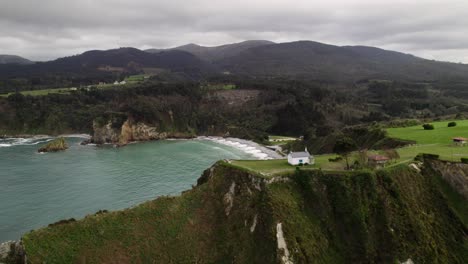 Flying-over-a-Chapel-in-the-border-of-a-sea-cliff-revealing-a-wild-beach-in-the-north-of-Spain