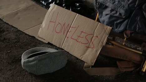 Close-Up-Shot-of-a-Homeless-Cardboard-Sign-with-a-Money-Hat-in-Front