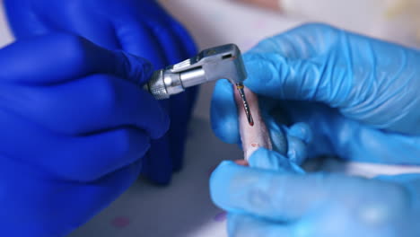 two pairs of hands in latex gloves holding drill machine and bone. drill is used to make a hole and red liquid appears. close up.