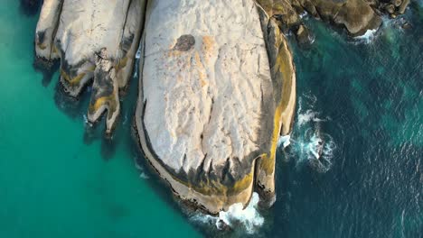 Olas-Azules-Del-Océano-Rompiendo-En-Grandes-Rocas-En-La-Playa-De-Llandudno-En-Ciudad-Del-Cabo,-Antena-De-Arriba-Hacia-Abajo