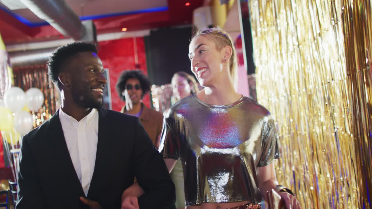 Video of diverse happy couple walking into nightclub arm in arm talking