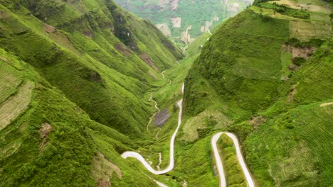Top-down-view-of-gorgeous-winding-road-carved-into-a-steep-lush-green-valley-in-the-mountains-of-northern-Vietnam