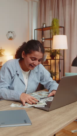 successful young woman freelancer using laptop celebrate success falling money at home office desk