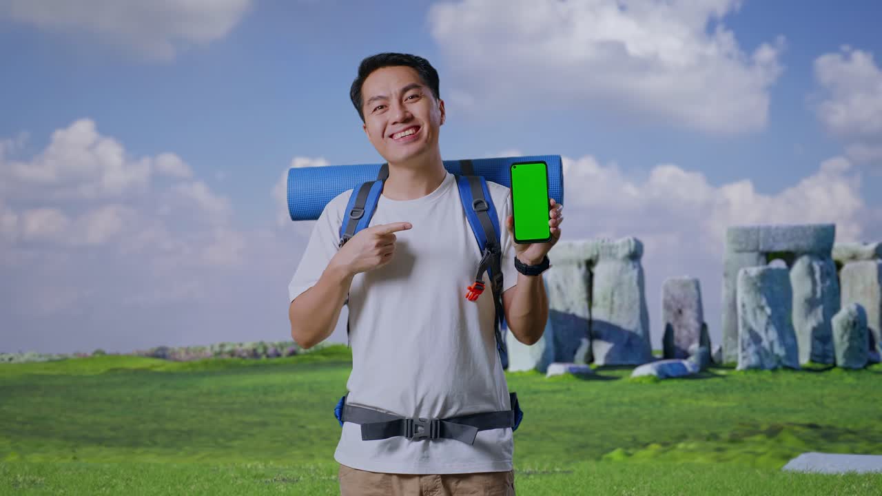 Smiling Tourist with Backpack Holding Green Screen Phone in Front of Stonehenge