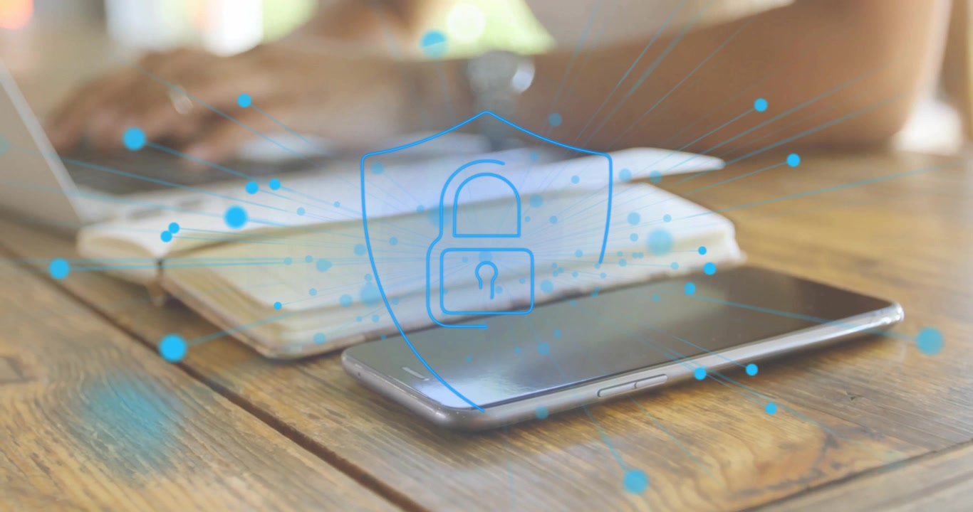 Particelle che formano un blocco scudo digitale sopra uno smartphone e un notebook, svanendo mentre una donna digita su un laptop.