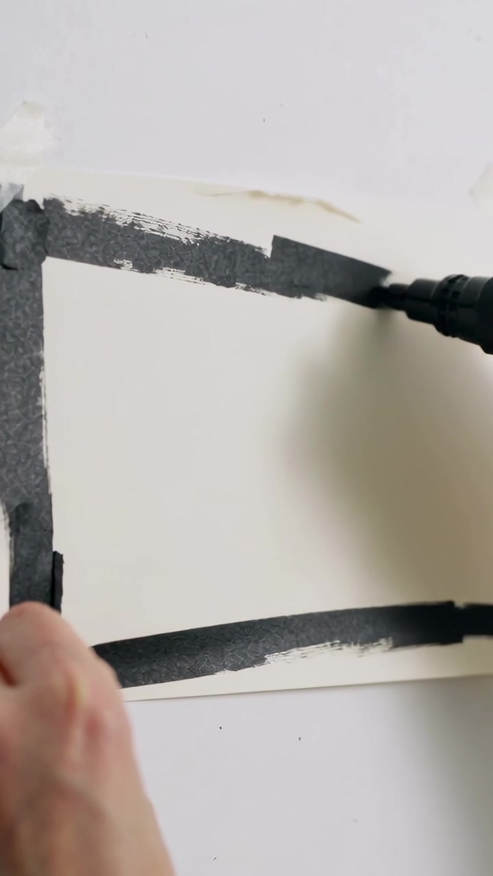 Video verticale: Mano ferma, artista che disegna un bordo con un pennarello nero spesso su carta fissata con nastro adesivo in una stanza