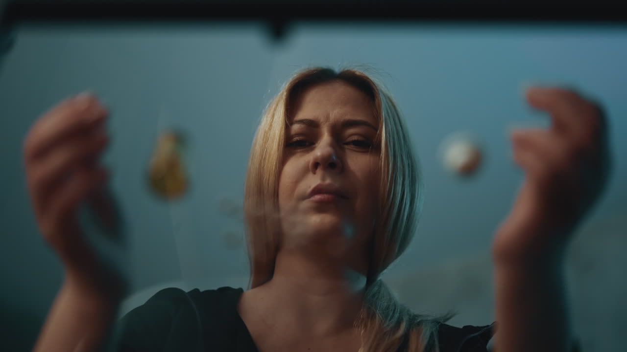 Lady sits at table with scattered pills in semi-dark room