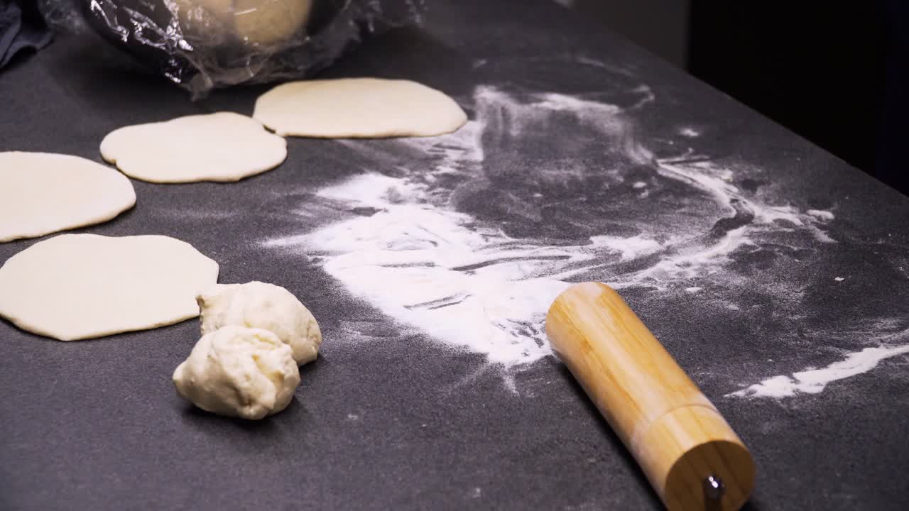 una foto de un hombre amasando pan en una gran mesa negra por la noche, preparando comida para la familia, de cerca