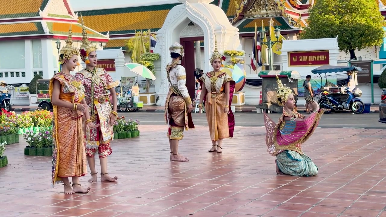 Para penampil dengan kostum berhias dan hiasan kepala emas menari di kuil Buddha bersejarah di Bangkok.