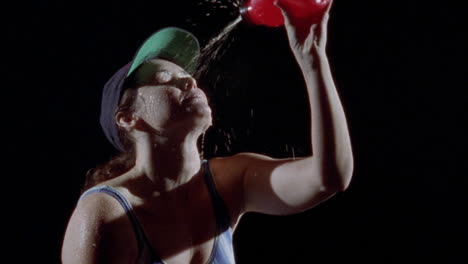 a woman pours water from a bottle over her face