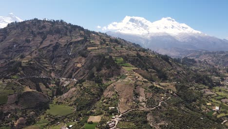 Beautiful-drone-shot-of-a-huge-green-hill-with-a-snow-peak-in-the-backround-in-the-highlands-of-Peru