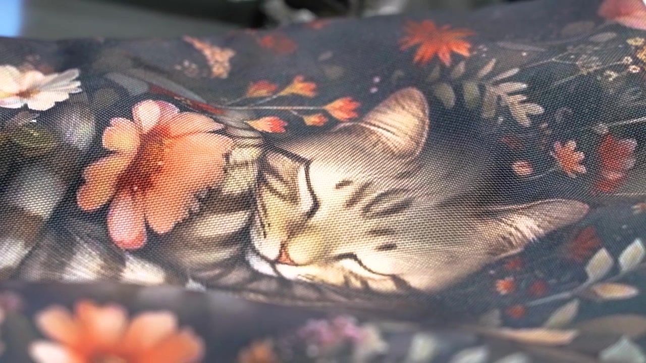 Primo piano di un tessuto floreale scuro con un motivo di gatti soriani addormentati che si muove nel vento