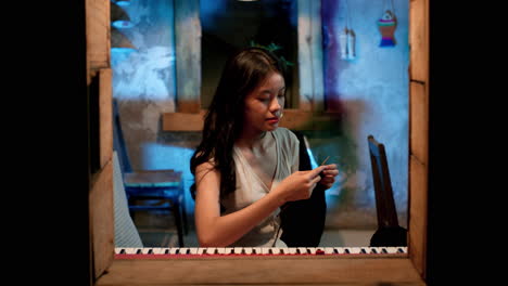 asian girl crocheting at the window, static