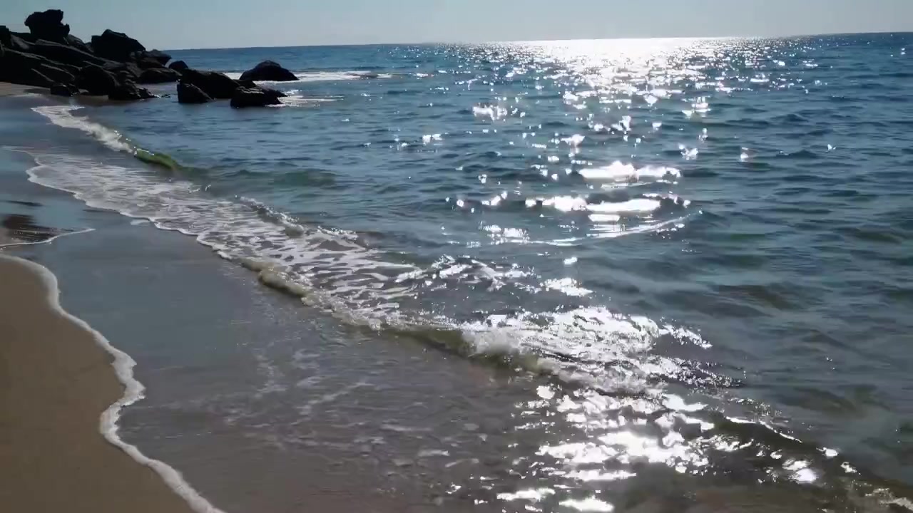 Onde delicate che si infrangono su una spiaggia sabbiosa con il luccichio del sole