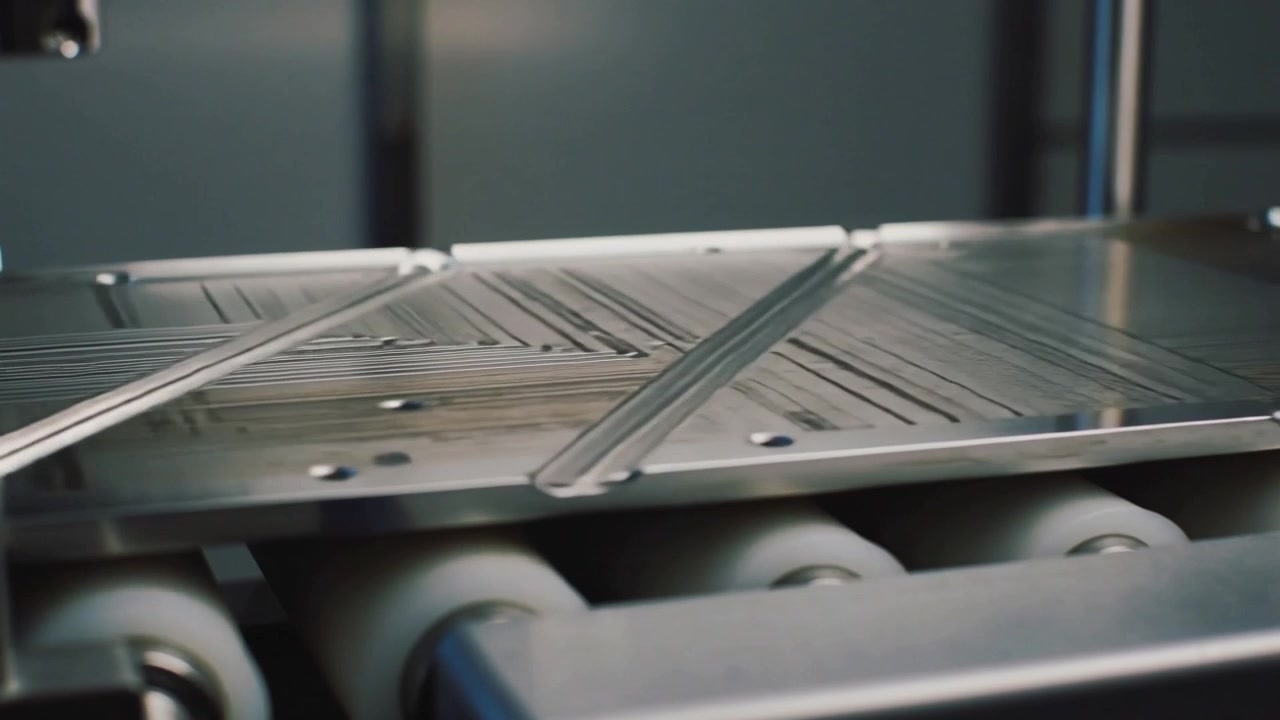 Advancing metal panel on rollers, conveyor moving, nozzle laying diagonal fine beads for coating