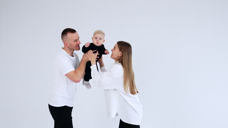 happy loving parents play with their adorable chubby baby. mom and dad try to entertain their serious kid. white backdrop.