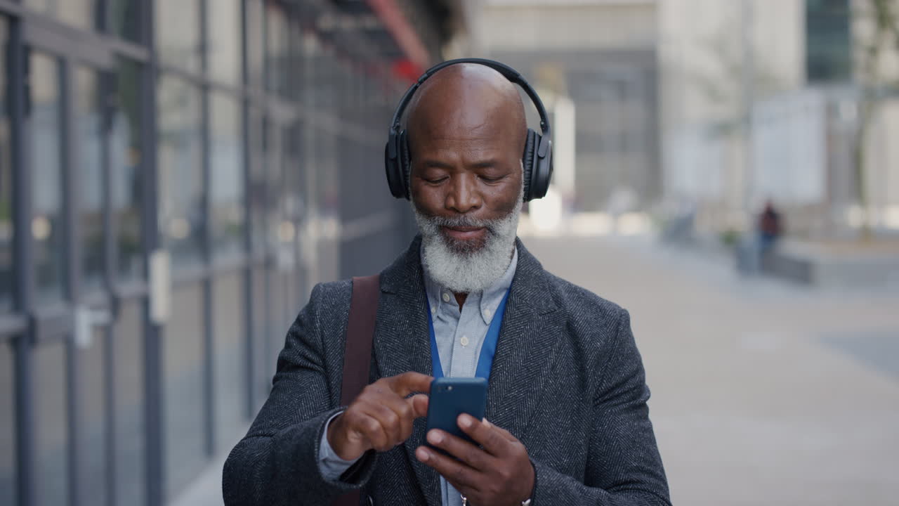 retrato de un empresario afroamericano de alto nivel que usa un teléfono inteligente en la ciudad disfrutando de escuchar música usando auriculares navegando por mensajes en línea enviando mensajes de texto en teléfono móvil en cámara lenta