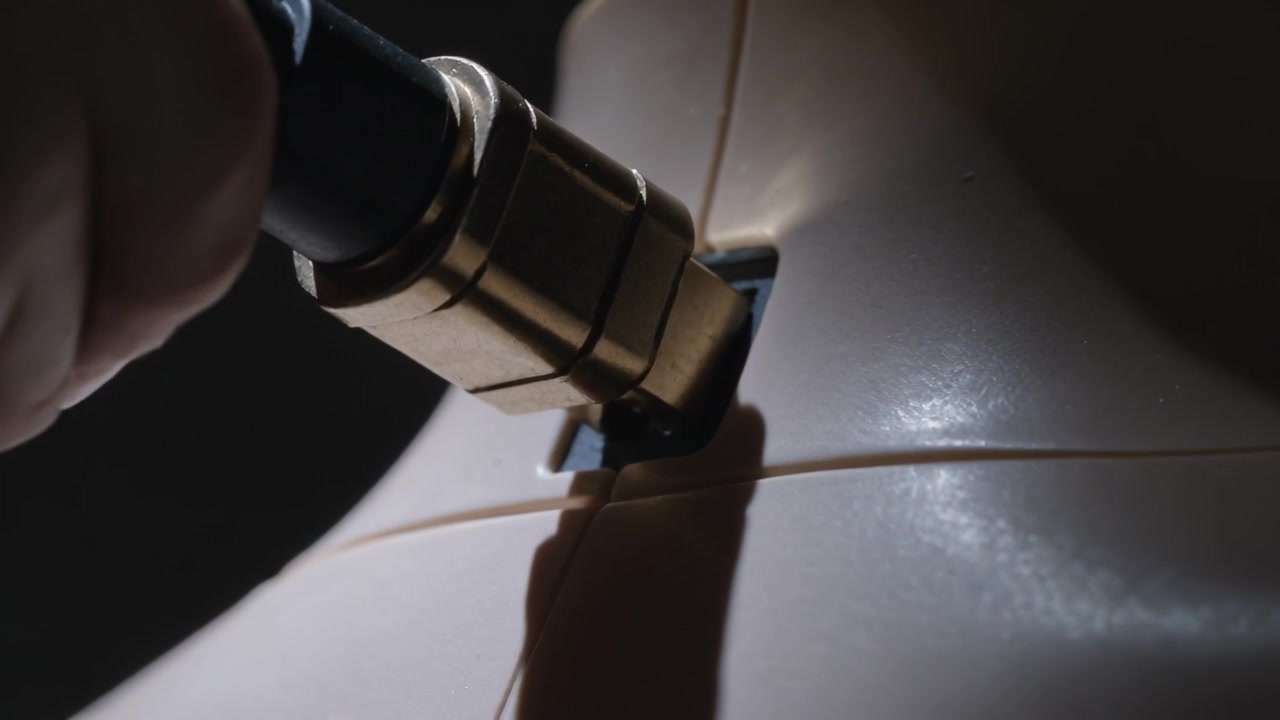 Main gantée insérant une fiche dorée dans une prise sur un boîtier beige, pour connecter un câble, la pointe métallique s'approchant.