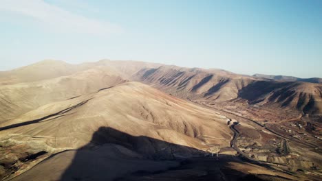 Paisaje-árido-De-Fuerteventura,-Caminos-Polvorientos-Que-Serpentean-A-Través-De-Colinas-Marrones-Yermas,-Cielo-Despejado,-Vista-Aérea